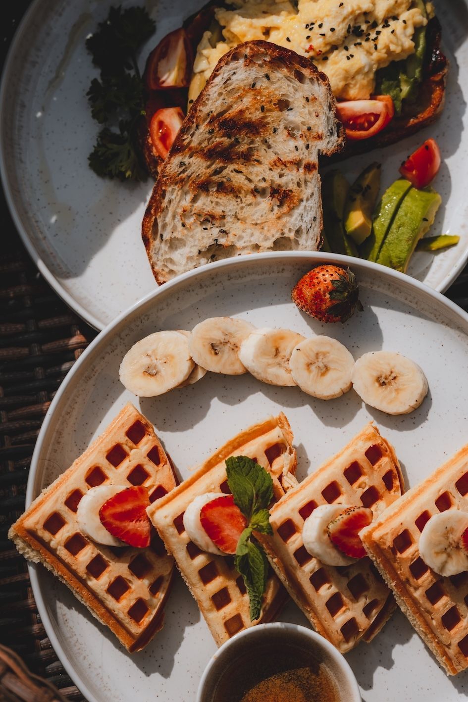 Plated waffles with banana slices and strawberries beside grilled chicken and vegetables