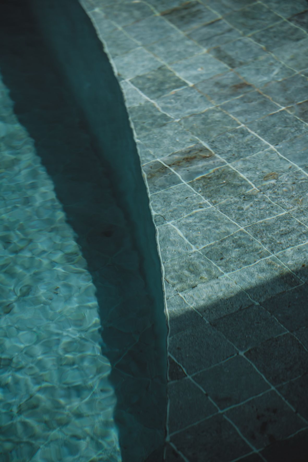 Pool edge with blue-tinted tiled steps and water, viewed from above