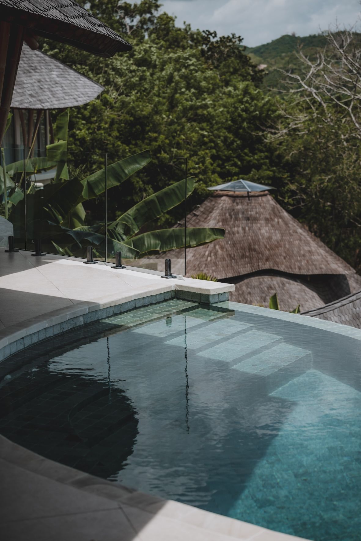 Infinity pool overlooking lush green hills and a thatched-roof hut