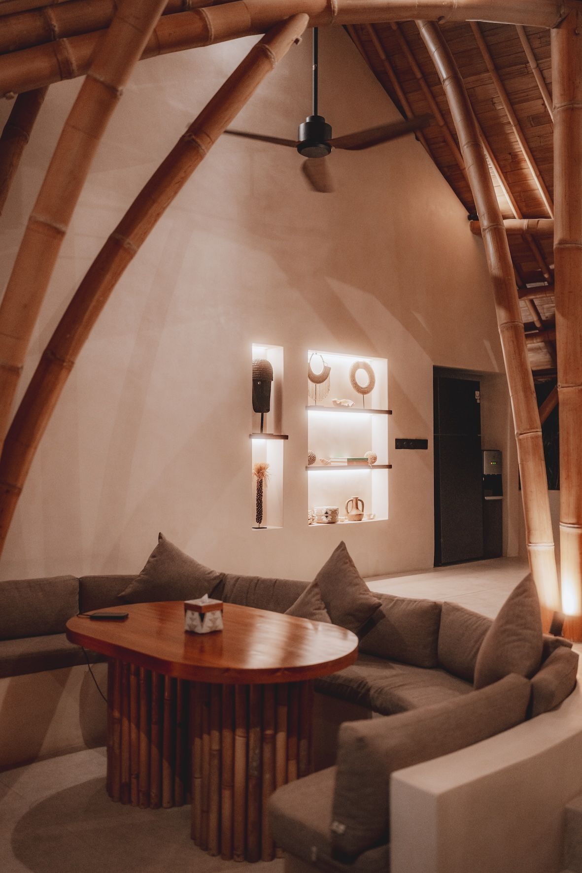 Cozy lounge with curved wooden beams, beige sofa, round table, and warm ambient lighting