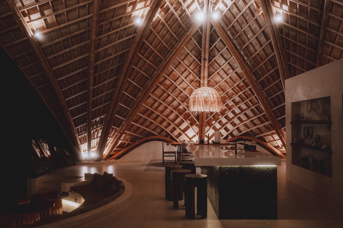 Warm-lit modern lounge with a high wooden A-frame ceiling and central chandelier.