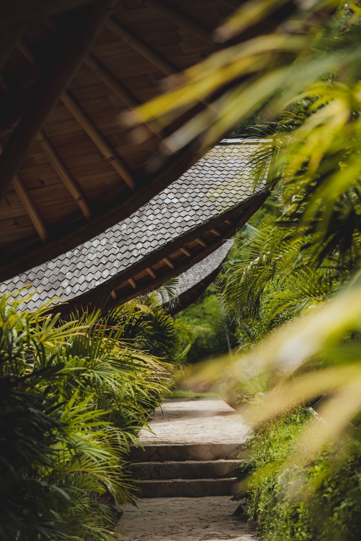 Stone path through lush green garden beside a thatched-roof pavilion