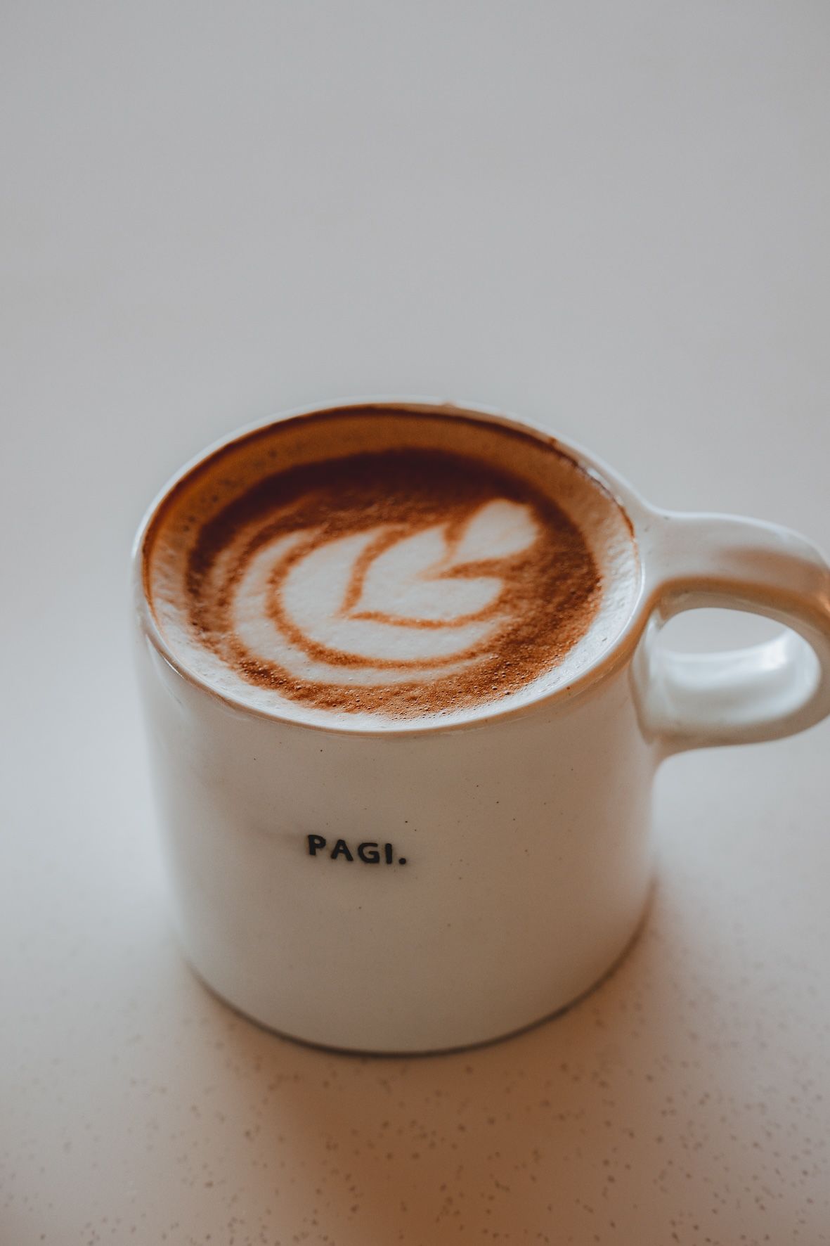 White coffee mug with latte art on a plain light background