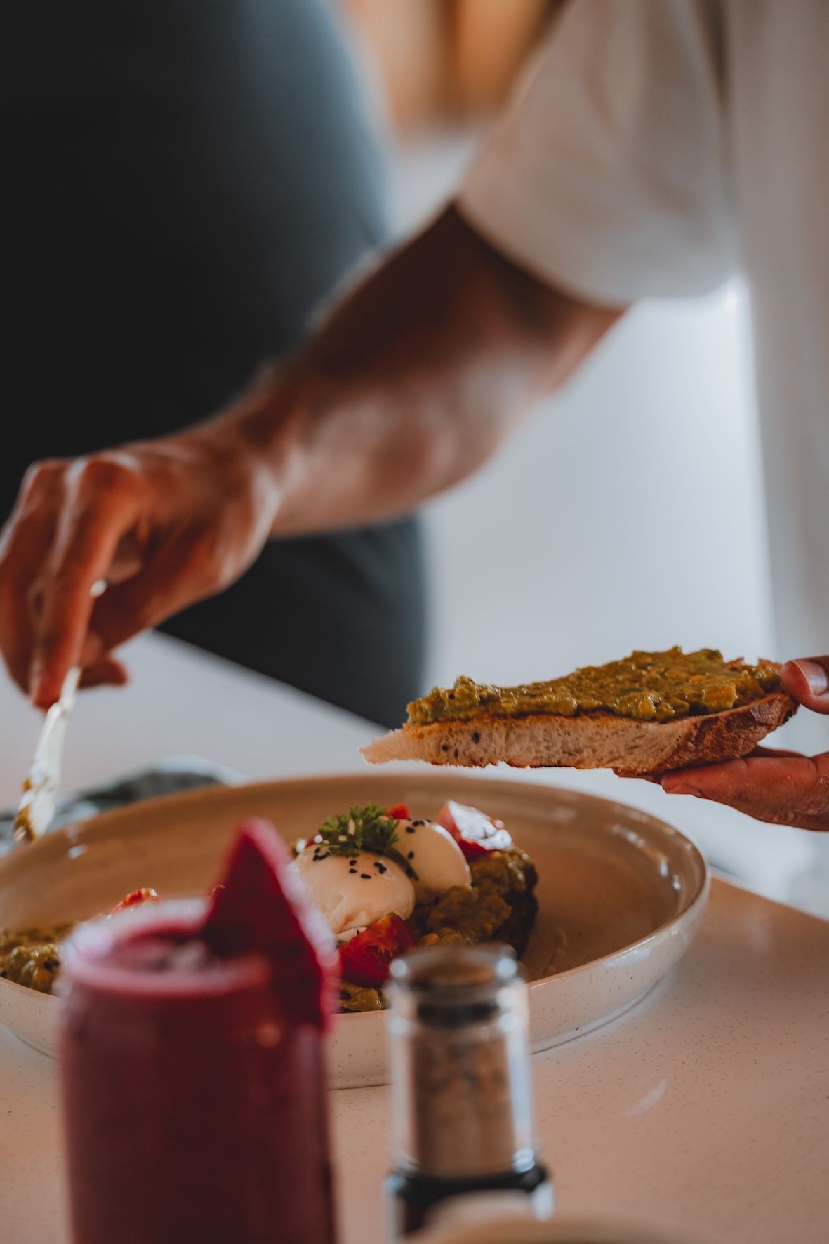 Hand placing garnish on a plated dish beside a slice of toast at a table