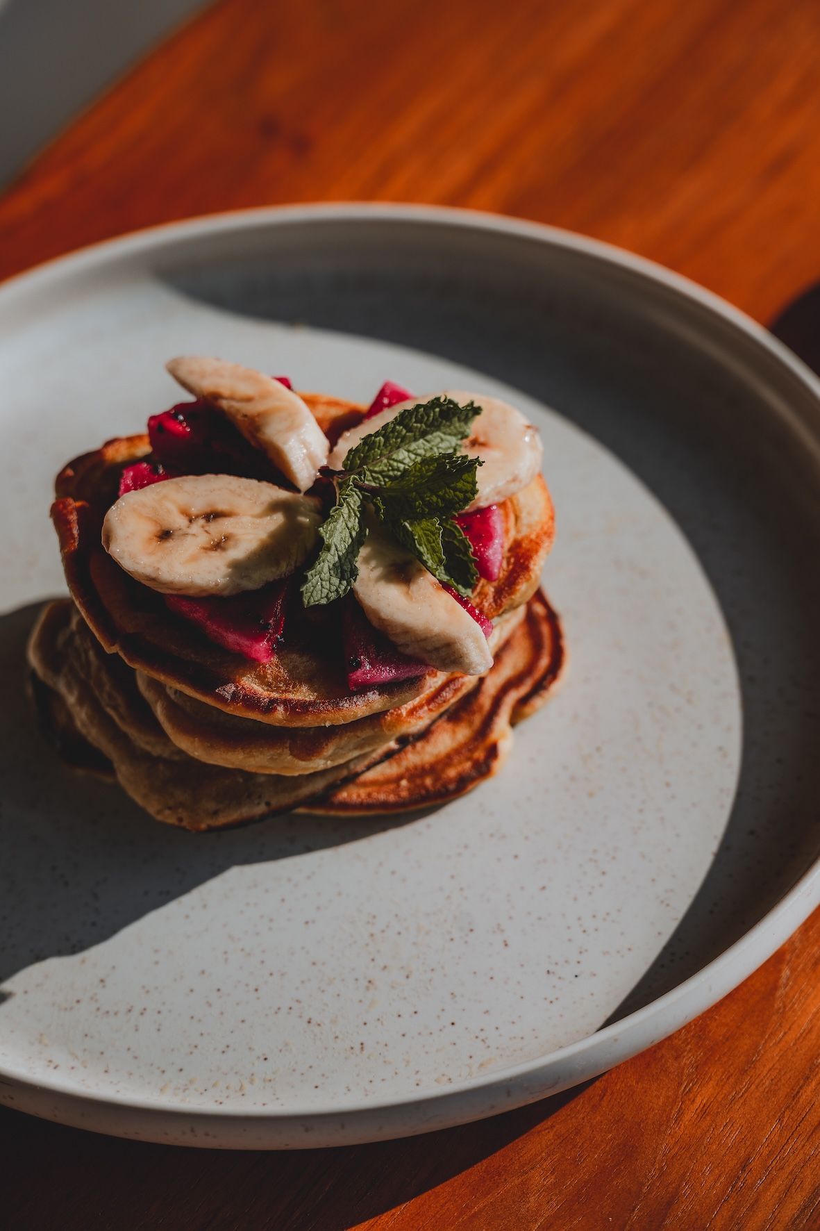 Pancakes topped with banana slices, berries, and mint on a gray plate