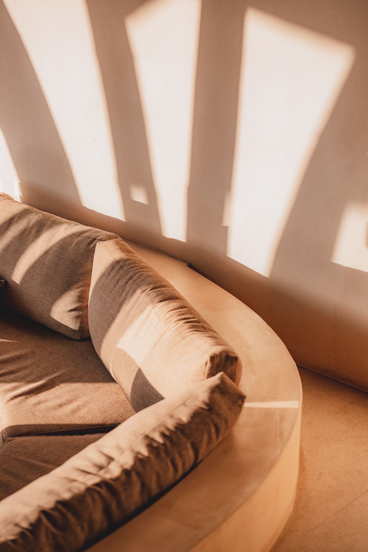 Sunlit beige sofa with patterned cushions against a wall casting window shadows
