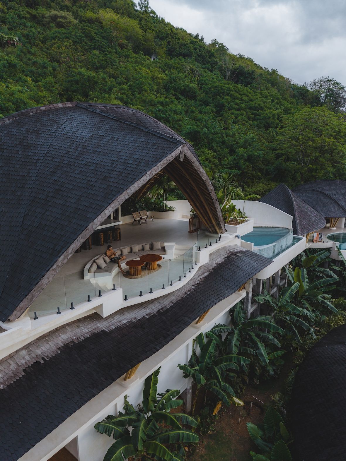 Modern building with a unique, curved roof, pool, and surrounding hillside.
