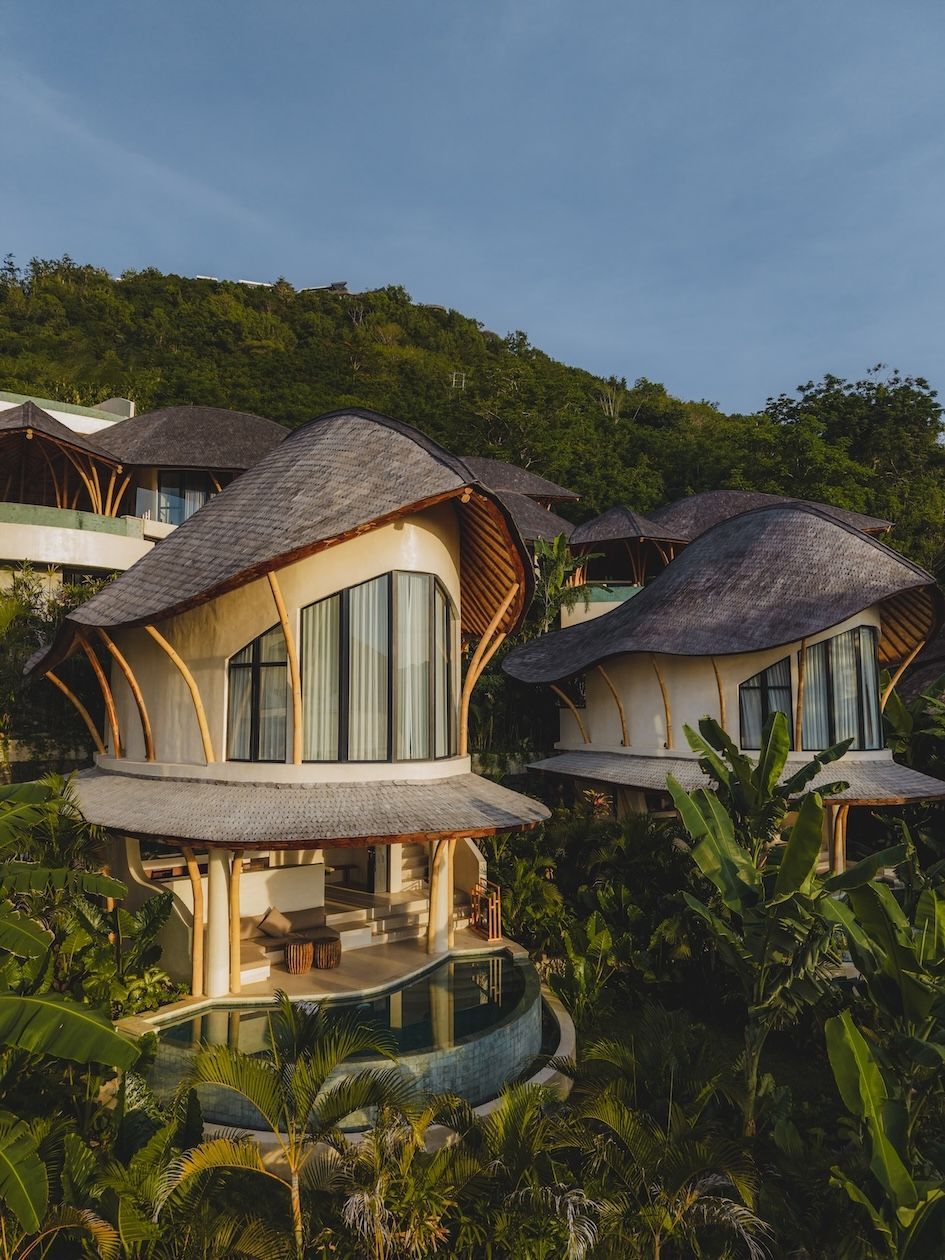 A unique bamboo-style house with a thatched roof, featuring a pool and surrounded by lush greenery.