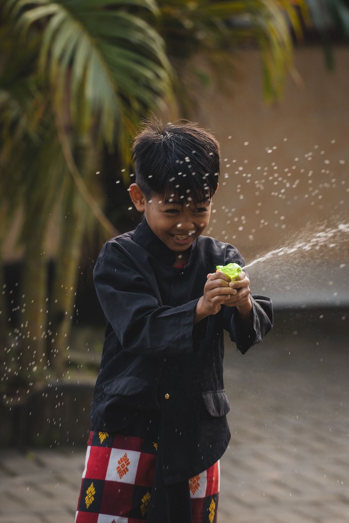 Child spraying water from a green toy outdoors, with water splashing around them.