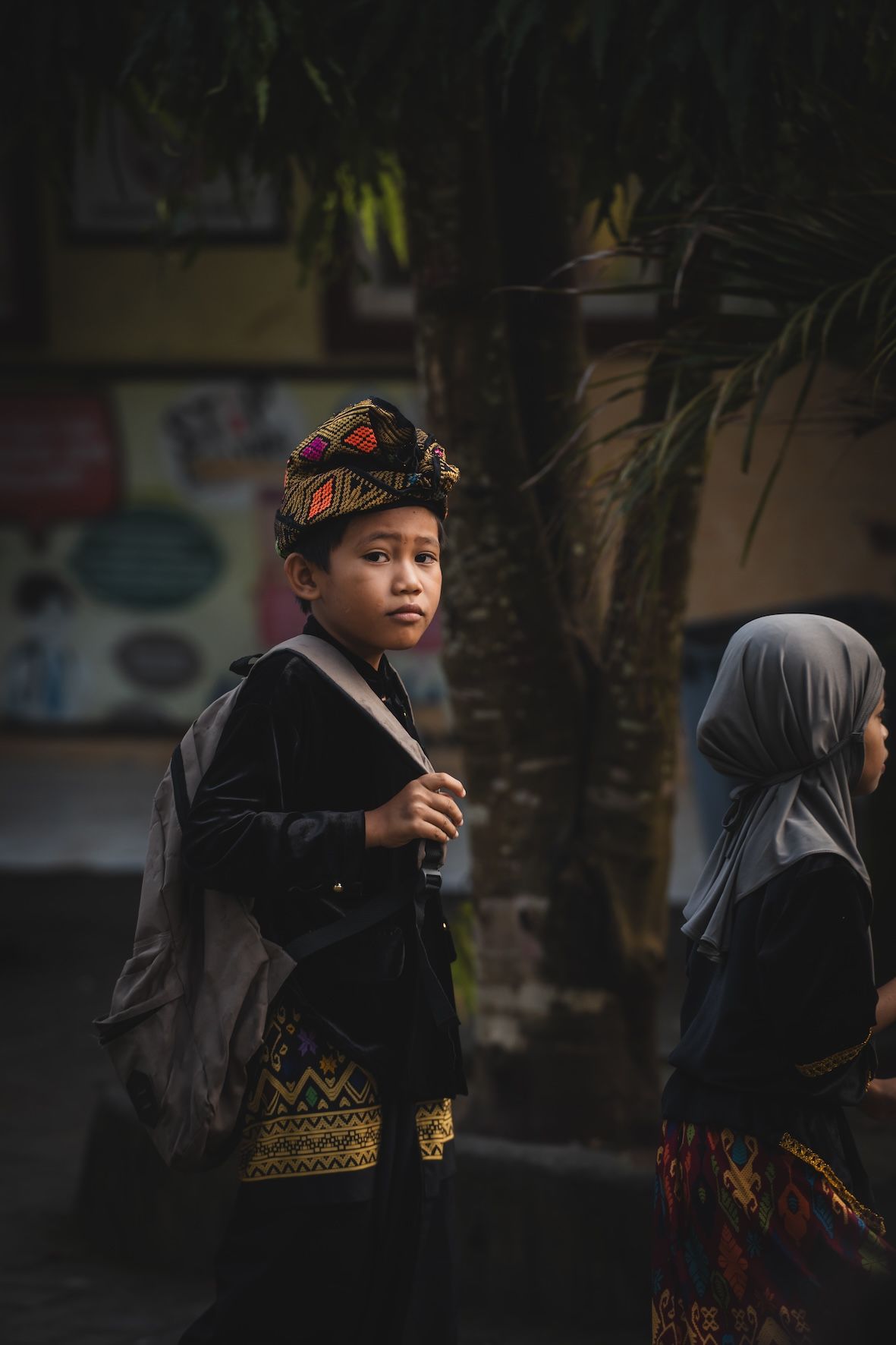 Two children outdoors, one wearing a floral headpiece and black clothing, in a dimly lit street scene
