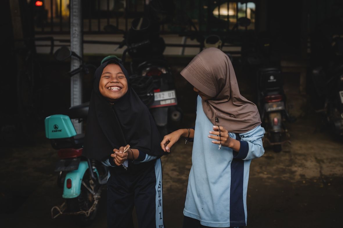 Two children smiling beside a teal scooter in a dim garage-like space
