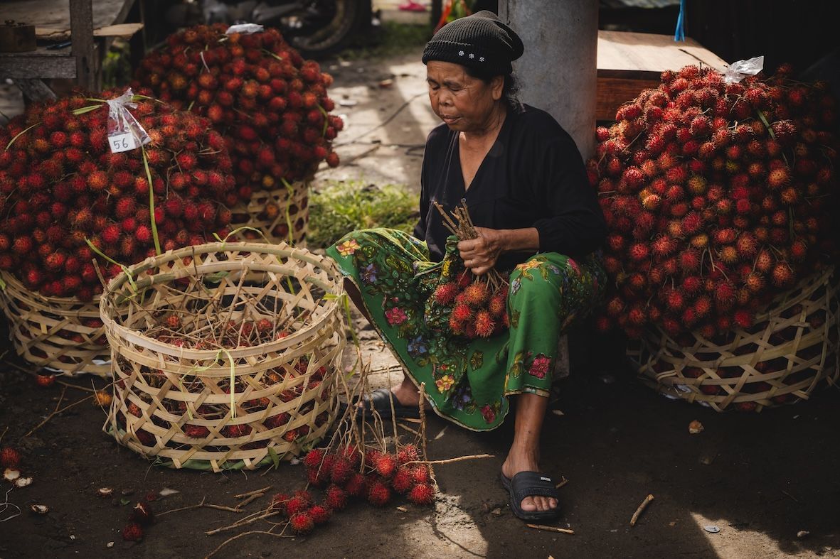 Vendor sitting amid baskets of red rambutan at an open-air market