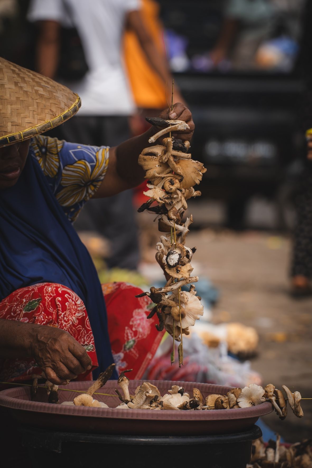 Street vendor in blue and red clothing grilling skewered meat beside a smoky fire.