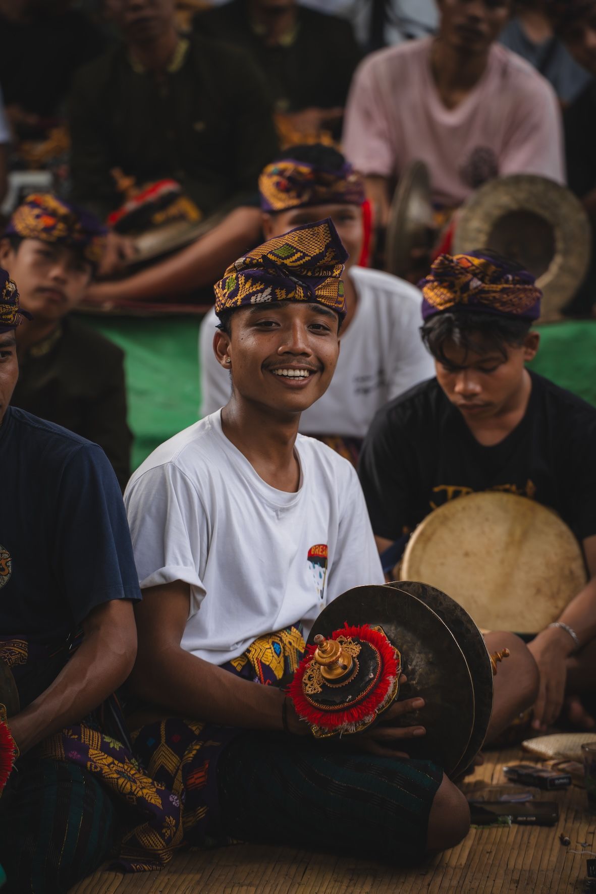 Group of musicians in traditional attire seated with cymbals and drums, smiling during a cultural performance.