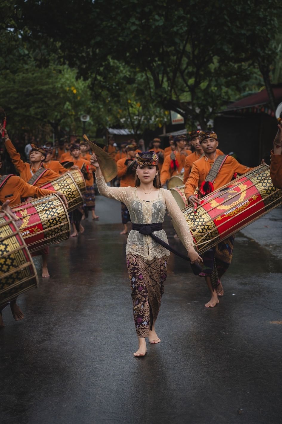 Traditional dancers in colorful costumes performing in the rain, with drums behind them.