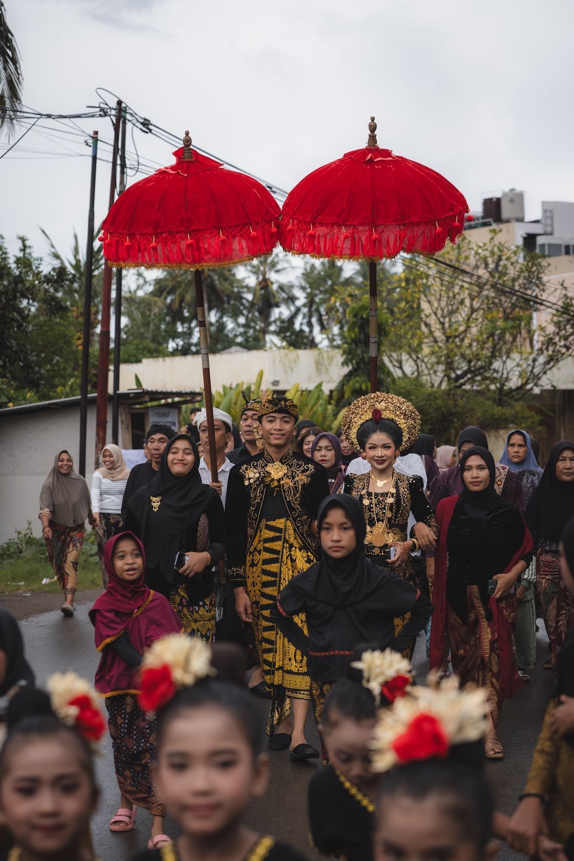 People in festive attire walking outdoors beneath red parasols during a procession