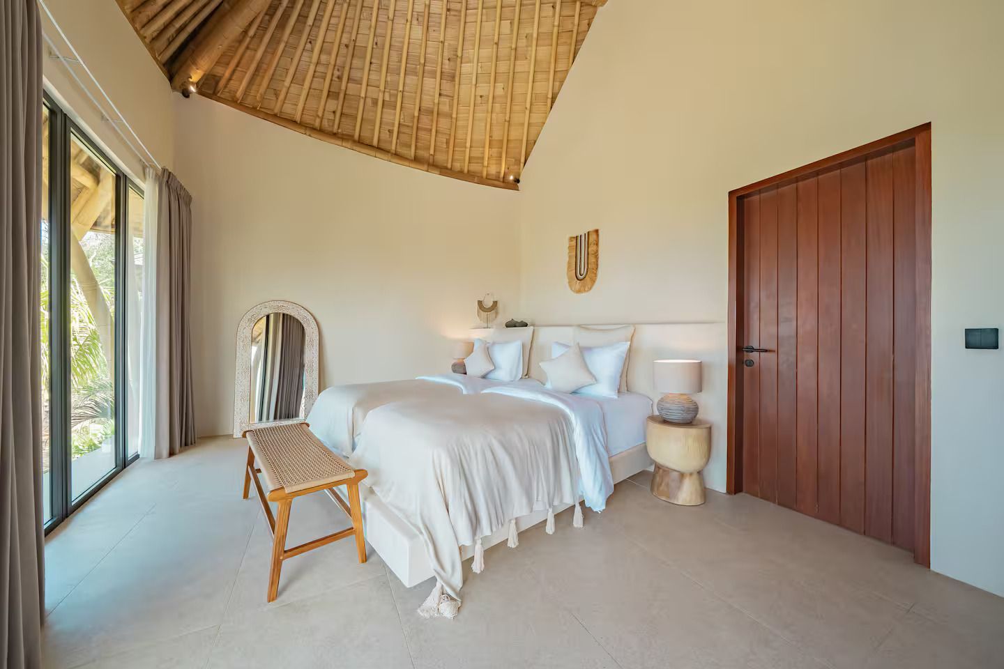 Bright bedroom with white bedding, wicker chair, large window, and wood closet door