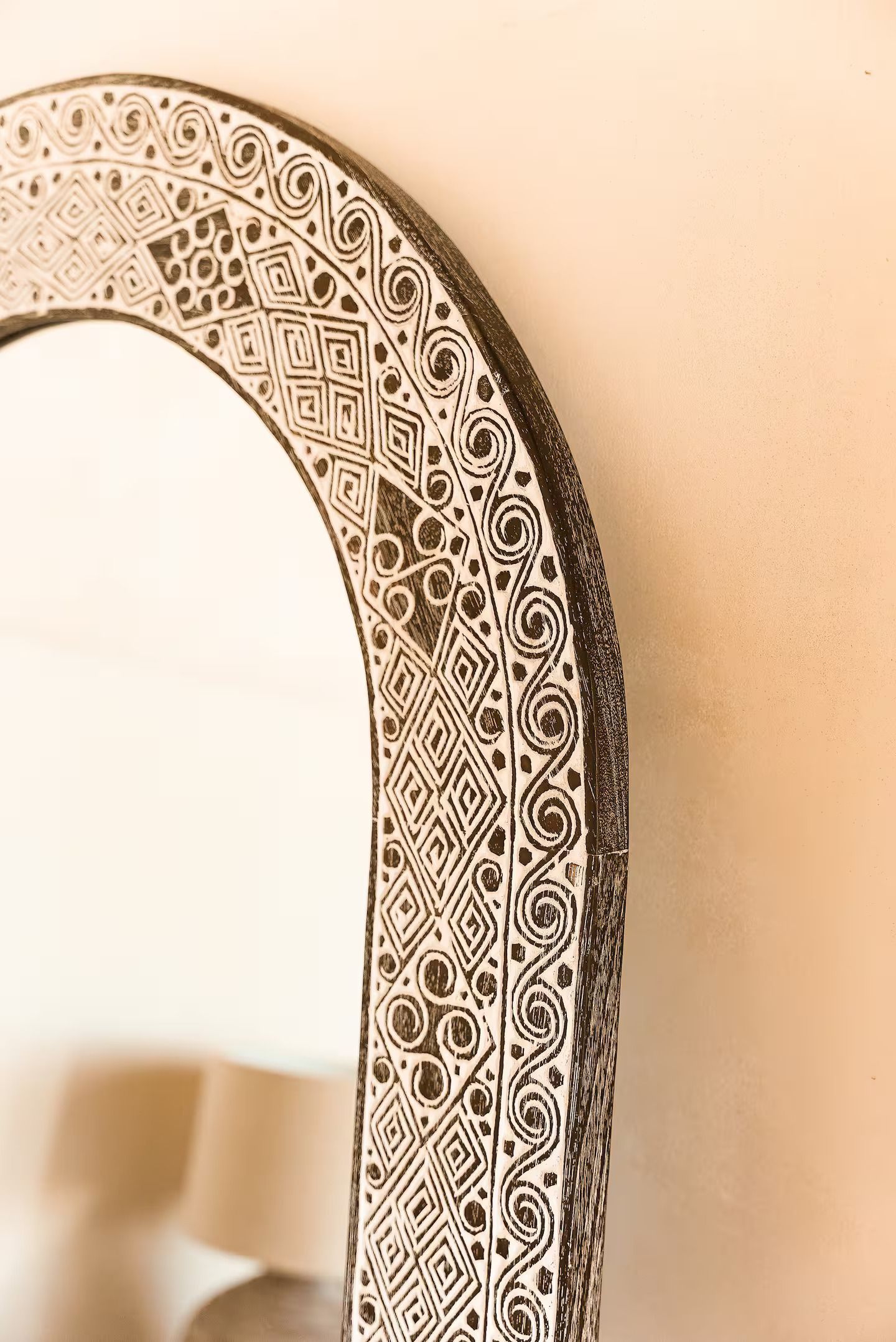 Ornate black-and-white round mirror on a beige wall, with a lamp reflected in it