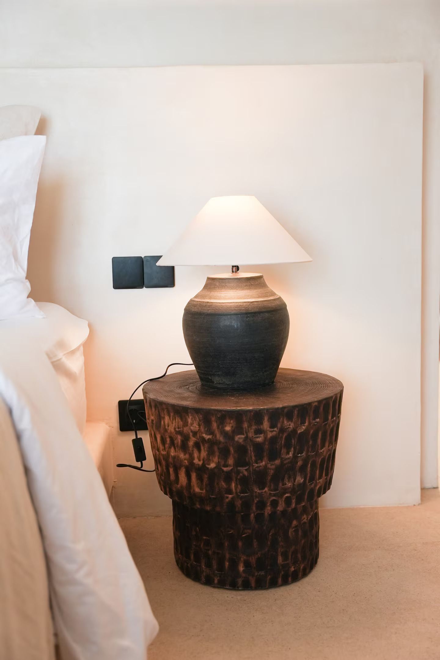 Nightstand lamp on a woven table beside a bed in a softly lit bedroom