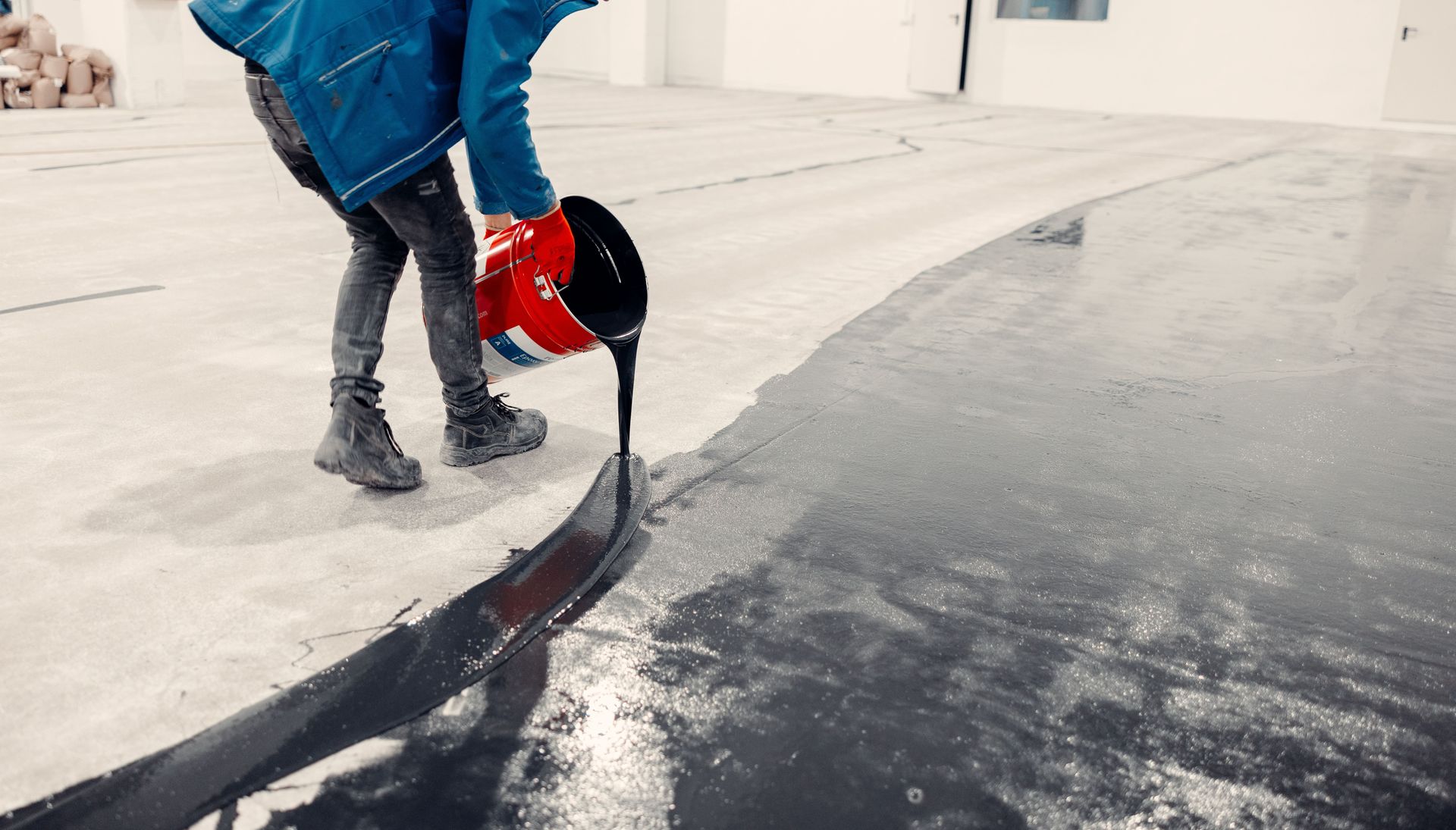 Person pours black epoxy from a bucket onto a concrete floor for a coating.
