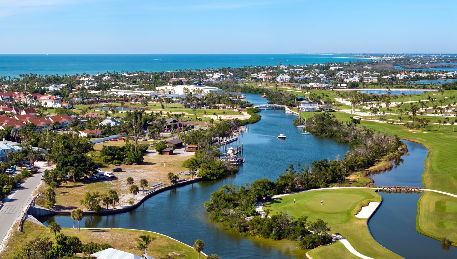 Aerial view of a coastal town with a waterway, golf course, and ocean under a blue sky. Aerial view of a coastal town with a waterway, golf course, and ocean under a blue sky.