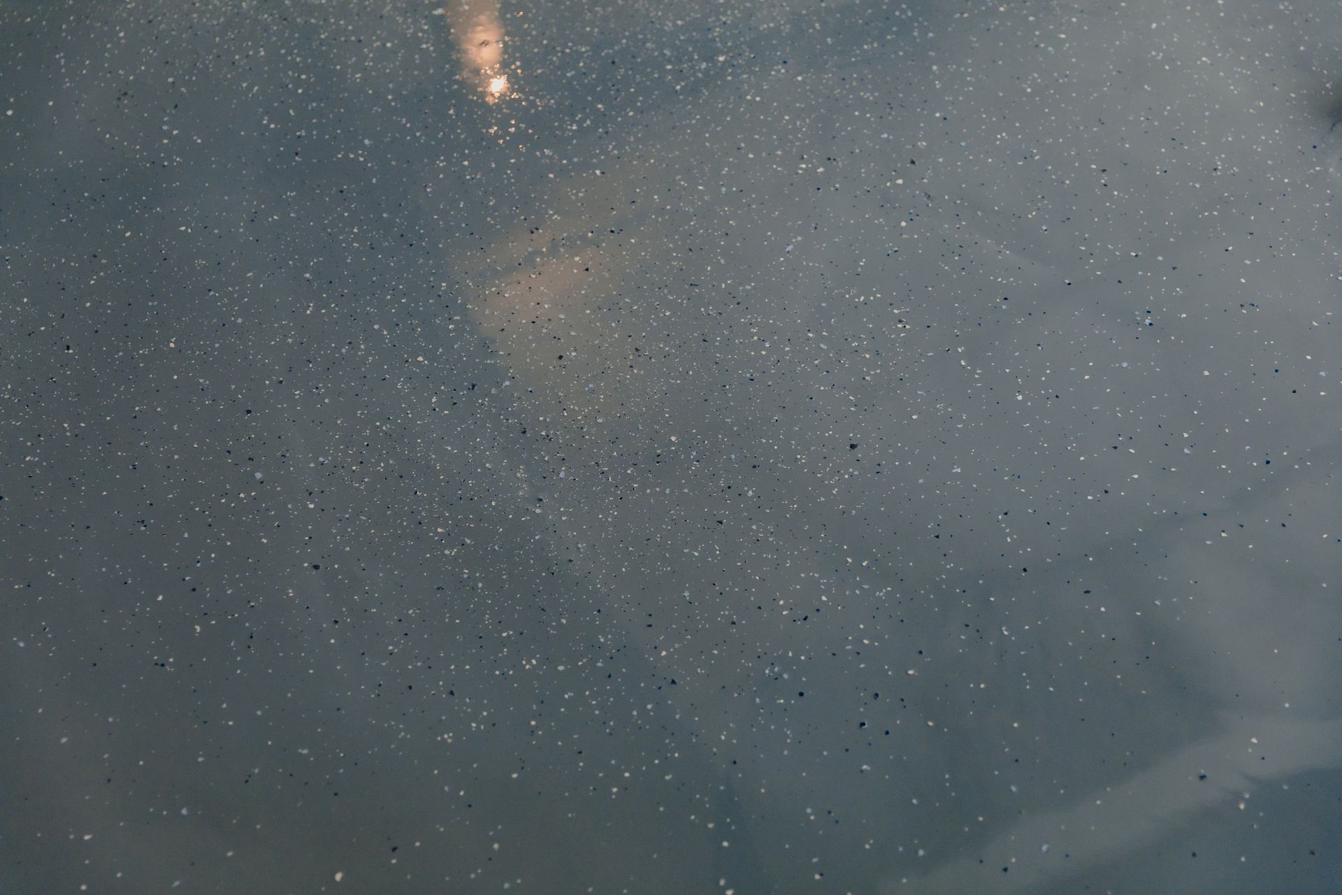 Dark gray surface speckled with tiny, bright dots. A blurred, lighter area is visible in the background. Dark gray surface speckled with tiny, bright dots. A blurred, lighter area is visible in the background.
