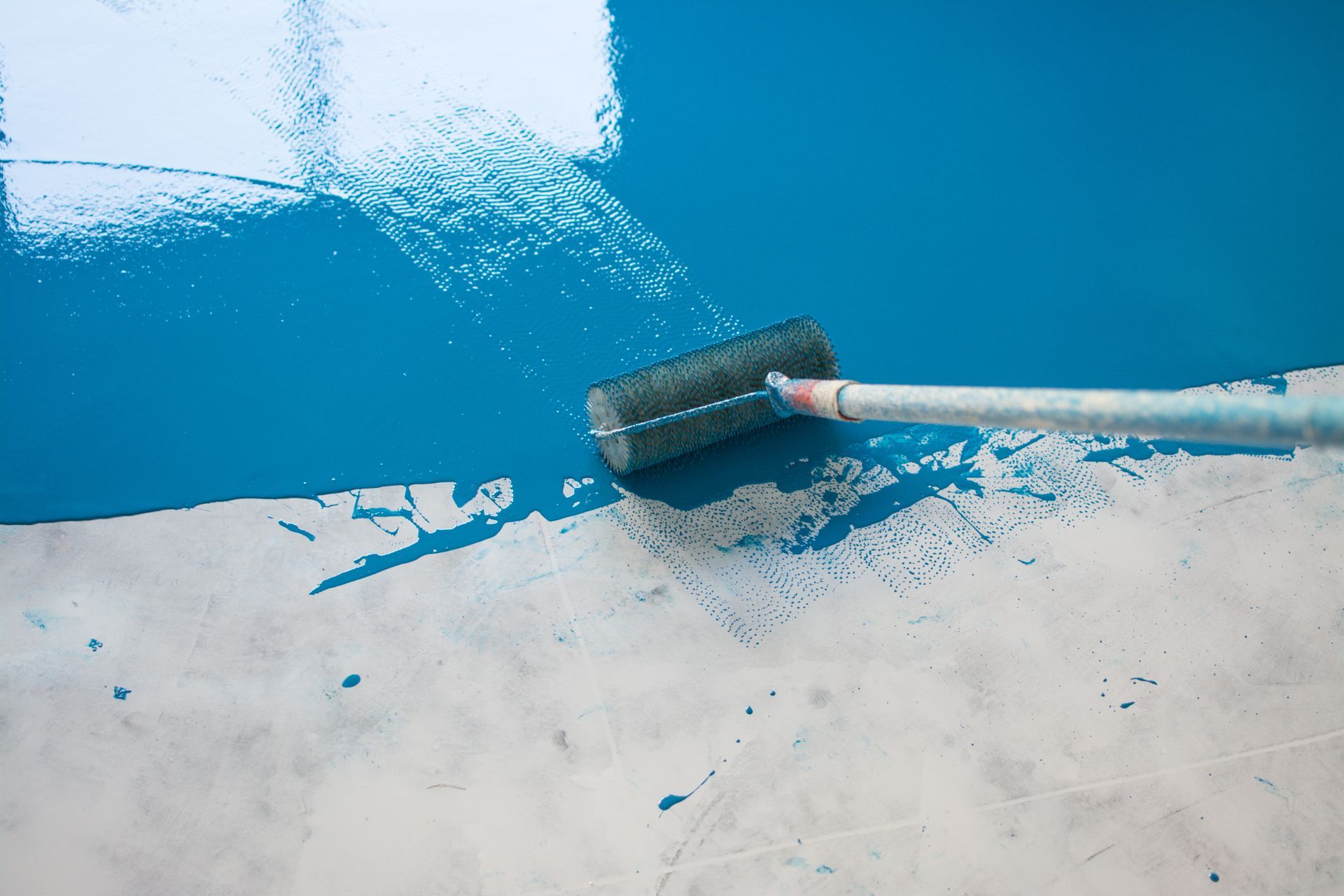 A paint roller applying blue paint to a concrete surface, with areas already painted and unpainted. A paint roller applying blue paint to a concrete surface, with areas already painted and unpainted.