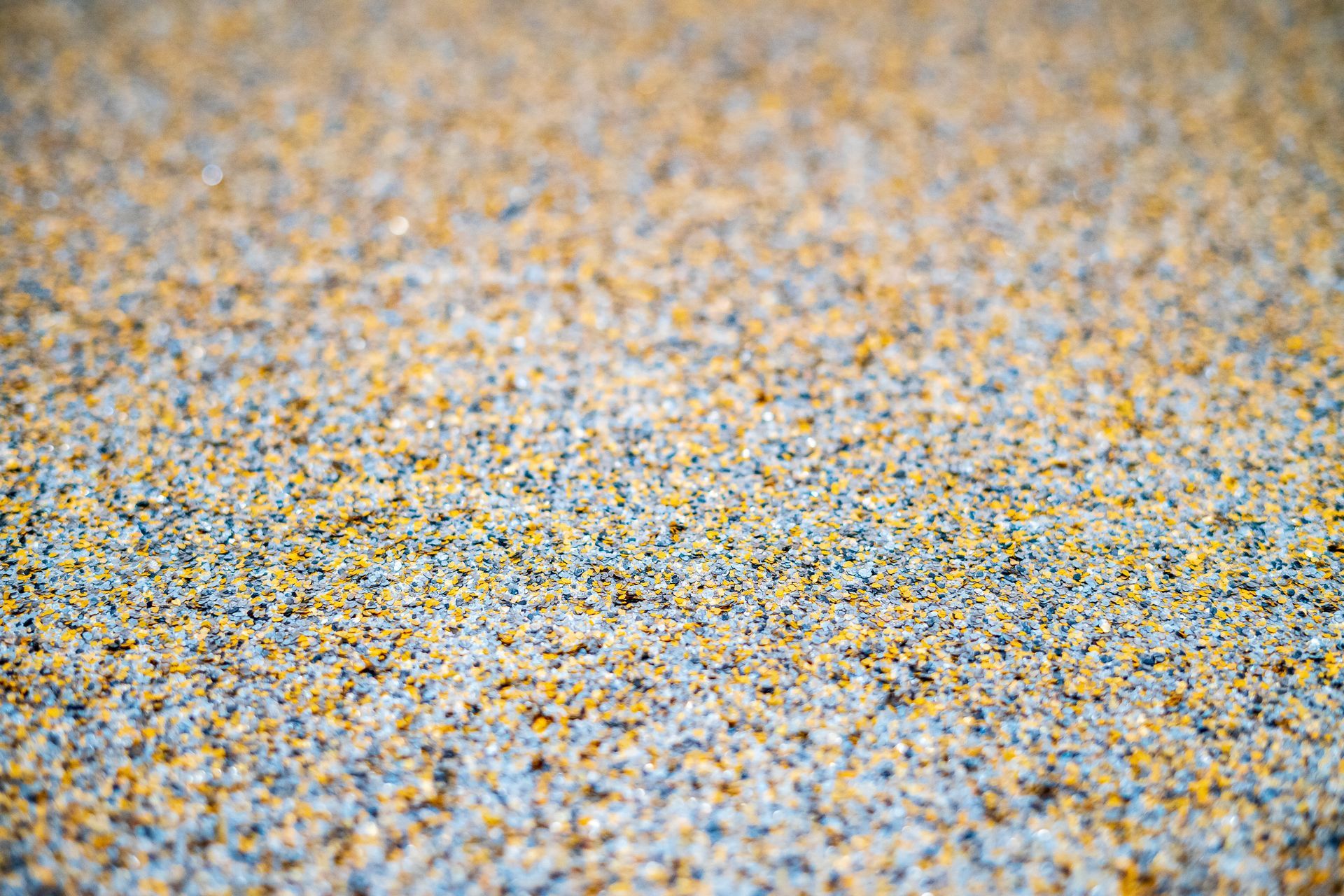 Close-up of a speckled, textured surface with blue, yellow, and gray grains. Close-up of a speckled, textured surface with blue, yellow, and gray grains.