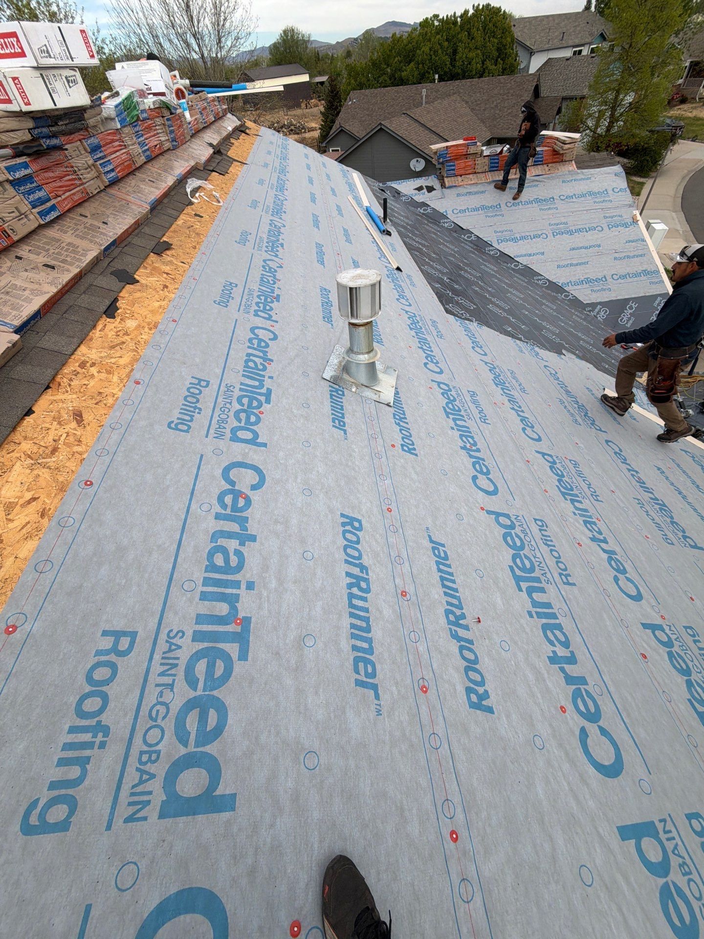 Roof under repair with workers installing weatherproof underlayment and vents on a sloped rooftop