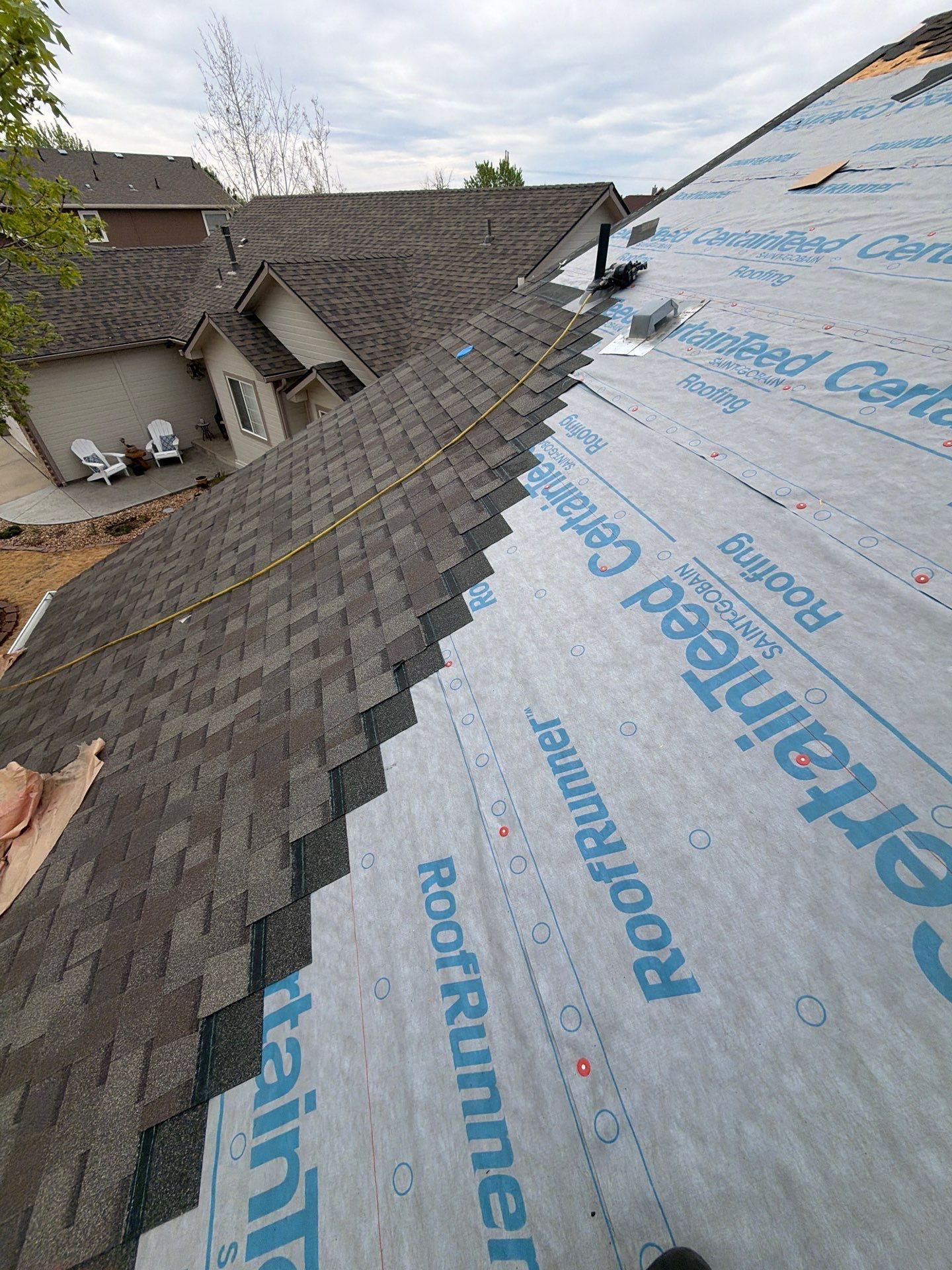 Roof under repair with exposed underlayment and shingles on a steep residential house roof