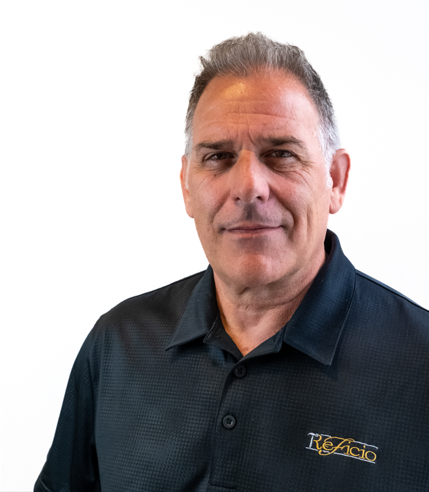 A middle-aged man with graying hair in a black polo shirt smiles slightly, looking directly at the camera. The setting appears to be indoors, against a white backdrop.