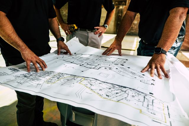 Two construction workers are looking at a blueprint and a tablet