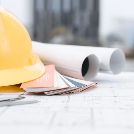Yellow hard hat sitting next to rolled up plans that are all sitting on blueprints
