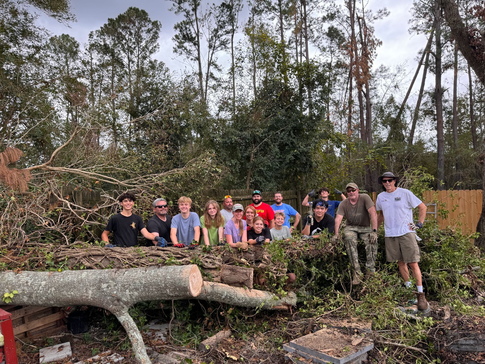 Group of people standing by a large fallen tree trunk in a wooded area, smiling after clearing debris.