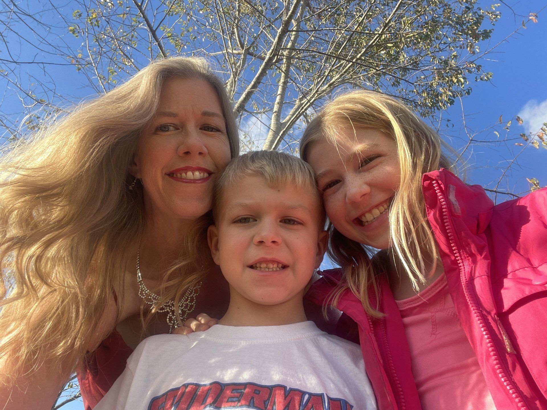 Woman and two children smile, posing for a photo outdoors.