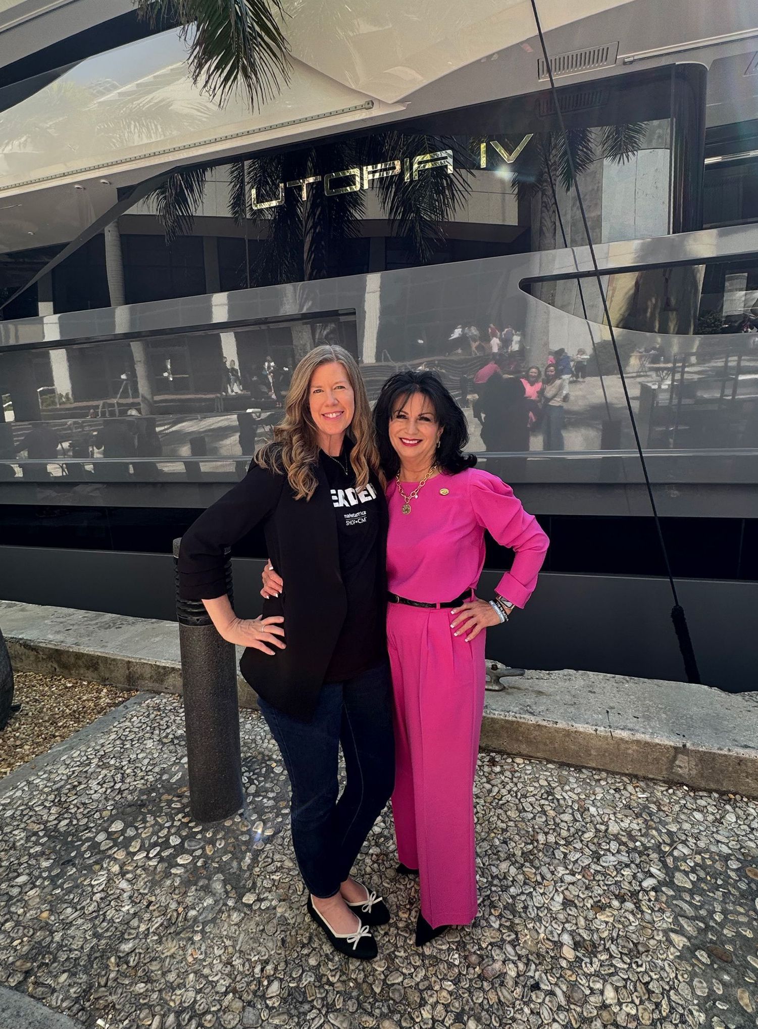 Two women pose in front of a yacht named 