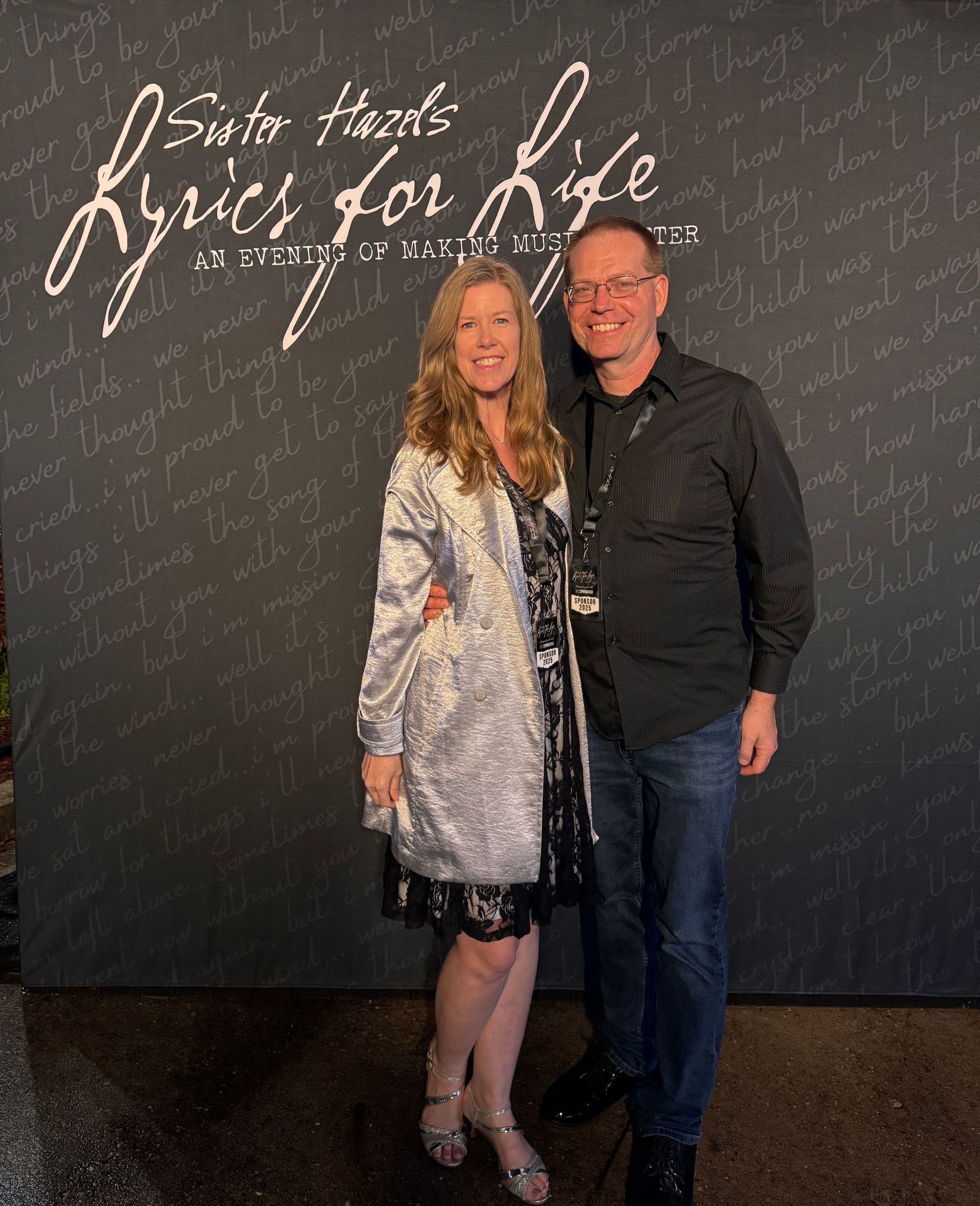 Couple posing in front of a ‘Lyrics for Life’ event backdrop.