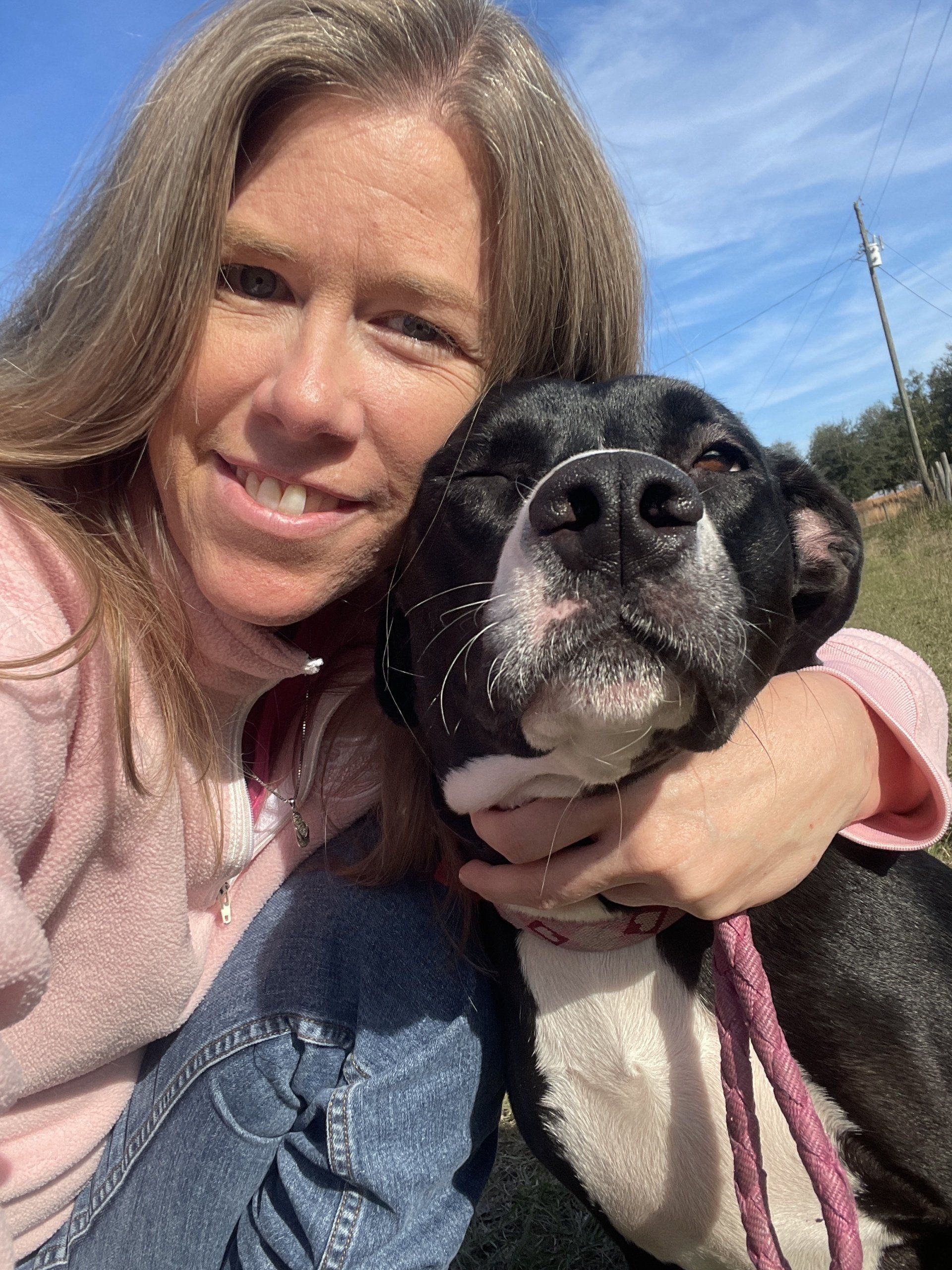 Woman hugging a black and white dog outdoors, smiling at the camera.
