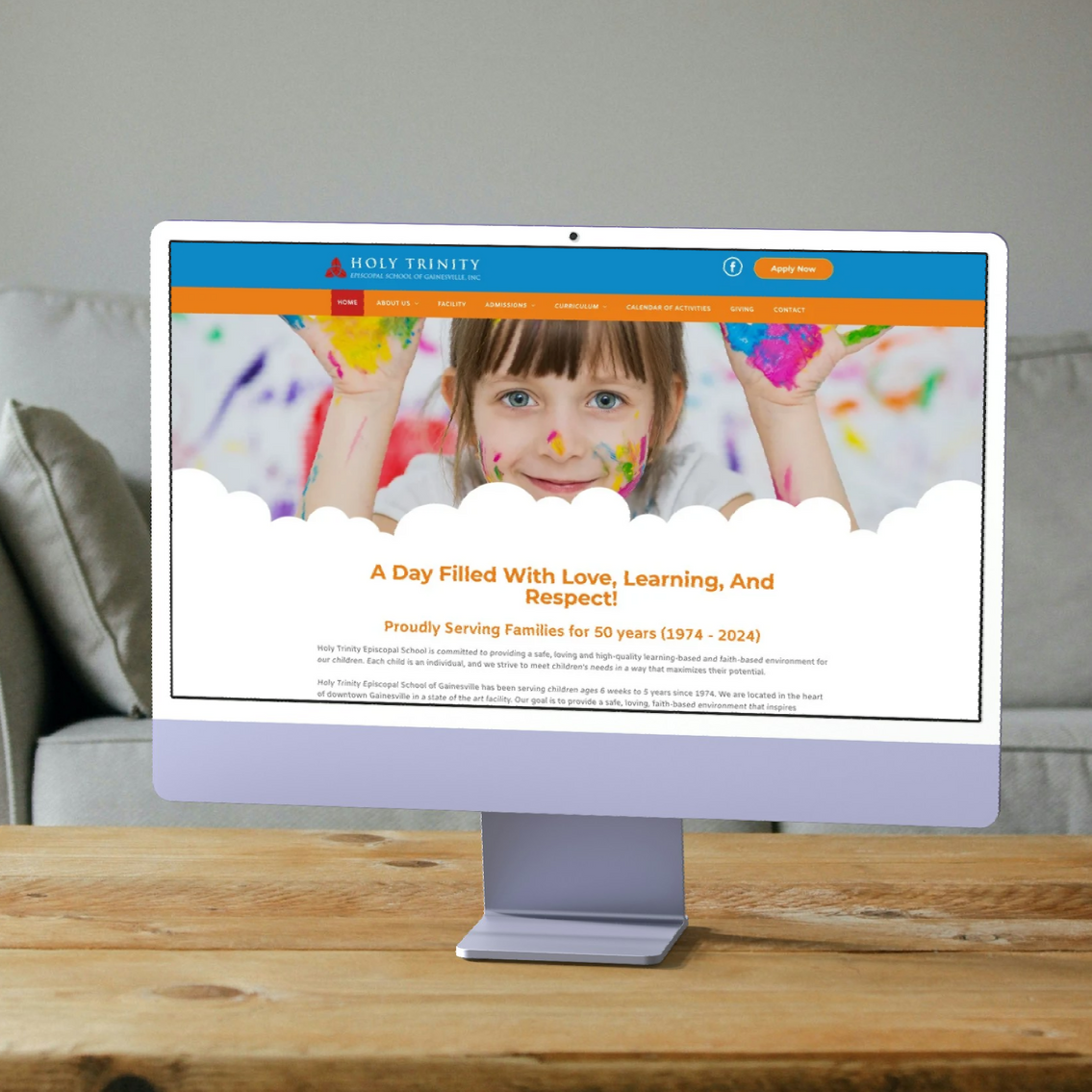 Desktop computer displaying a website with a child covered in paint. Wooden table, neutral background.
