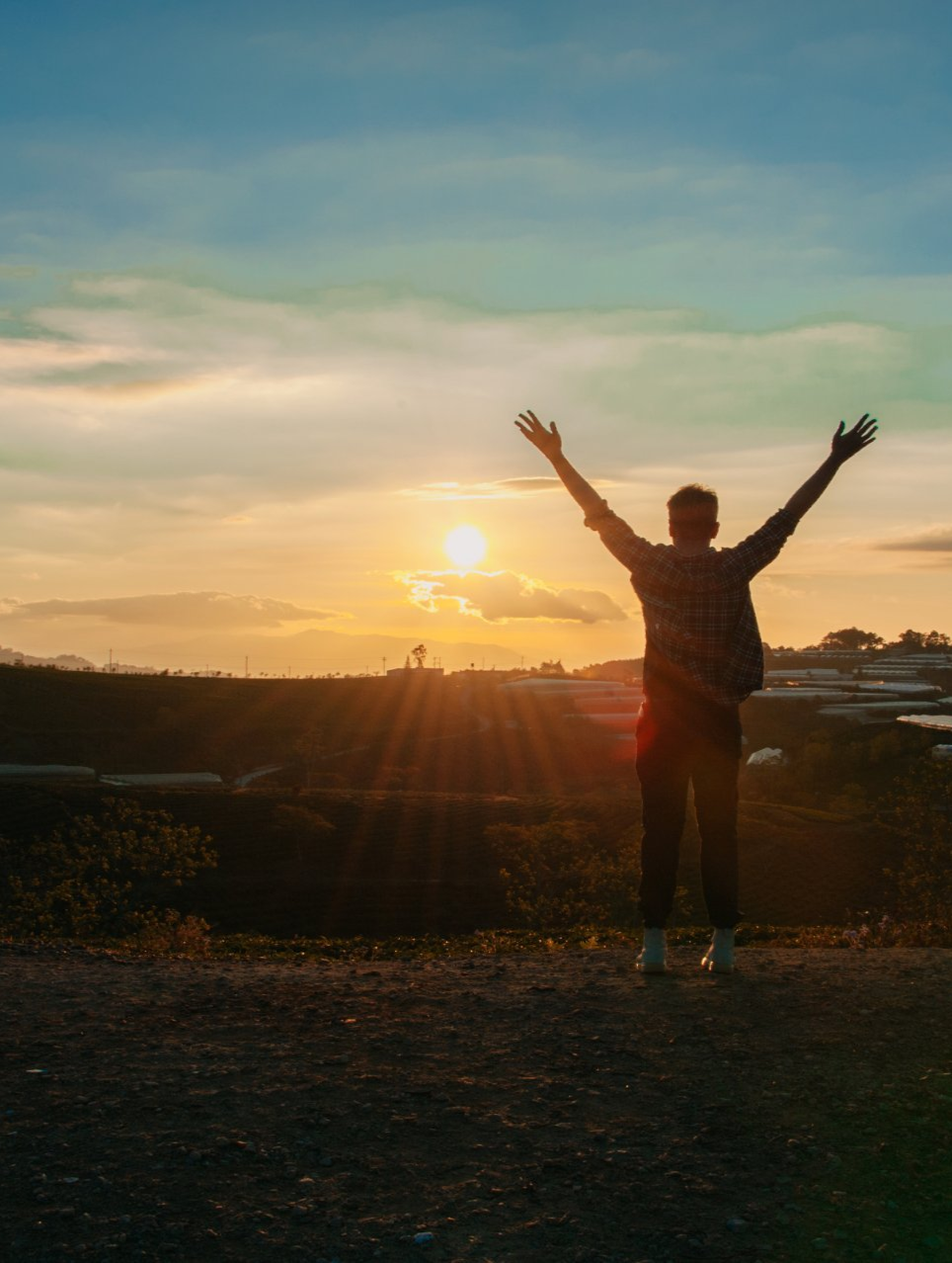 Person with arms raised towards a sunset, silhouetted on a hilltop. Golden light fills the sky.