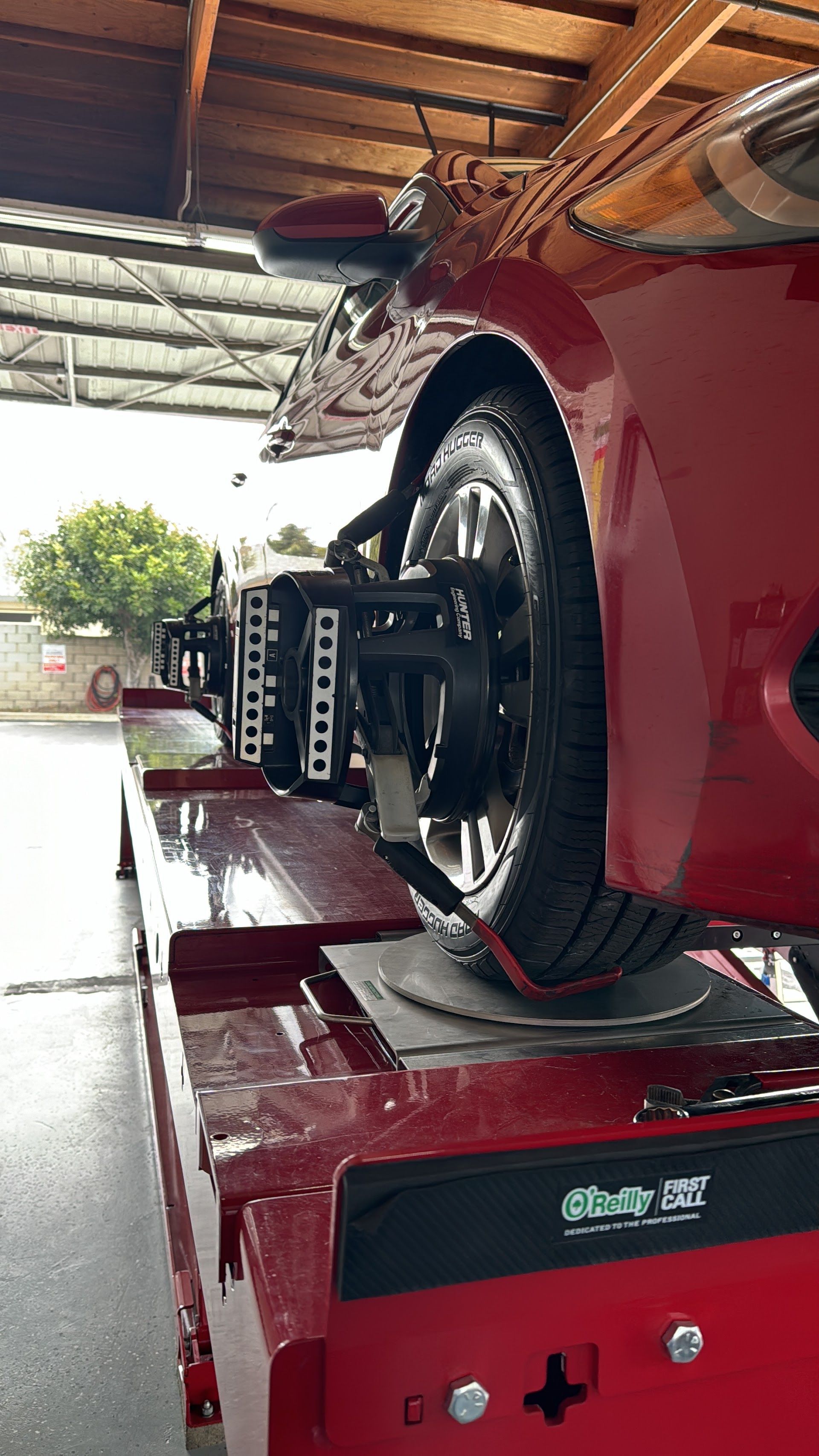 Red car on a vehicle lift in a garage, showing the wheel and undercarriage. | Top Alignment