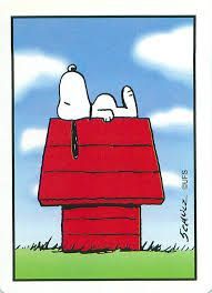Snoopy dorme in cima alla sua iconica cuccia rossa, sullo sfondo di un cielo azzurro punteggiato da soffici nuvole bianche.