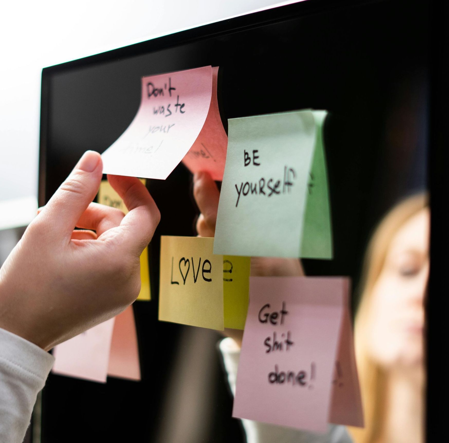 Una mano stacca un post-it rosa da una superficie scura, su cui si trovano anche altri bigliettini con scritto