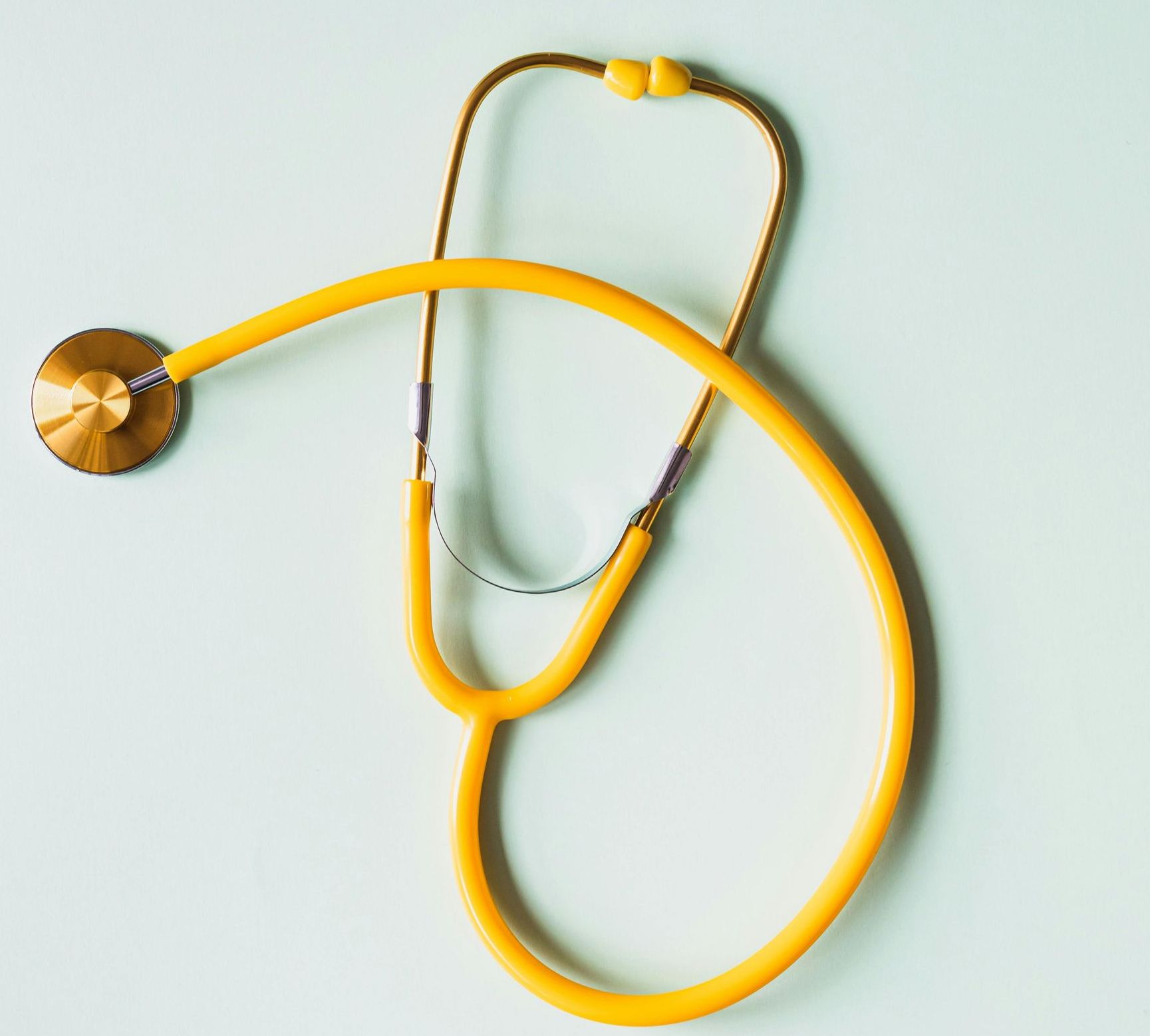 Uno stetoscopio medico giallo è posizionato su uno sfondo uniforme di colore chiaro.