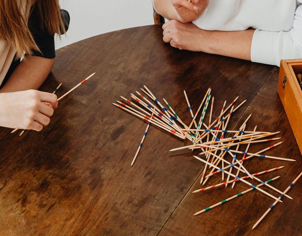 Due persone giocano a Mikado, un gioco di carte, su un tavolo di legno scuro.