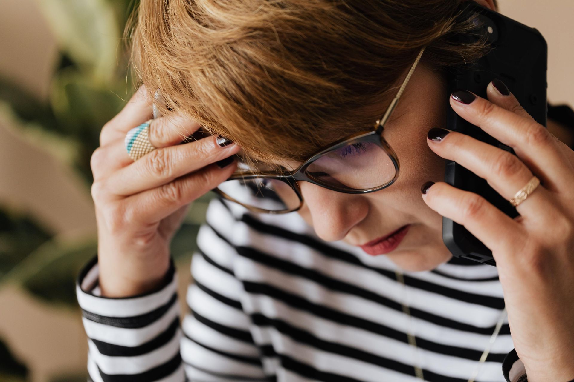 Una persona con una camicia a righe e gli occhiali tiene un telefono all'orecchio mentre guarda in basso con un'espressione preoccupata.