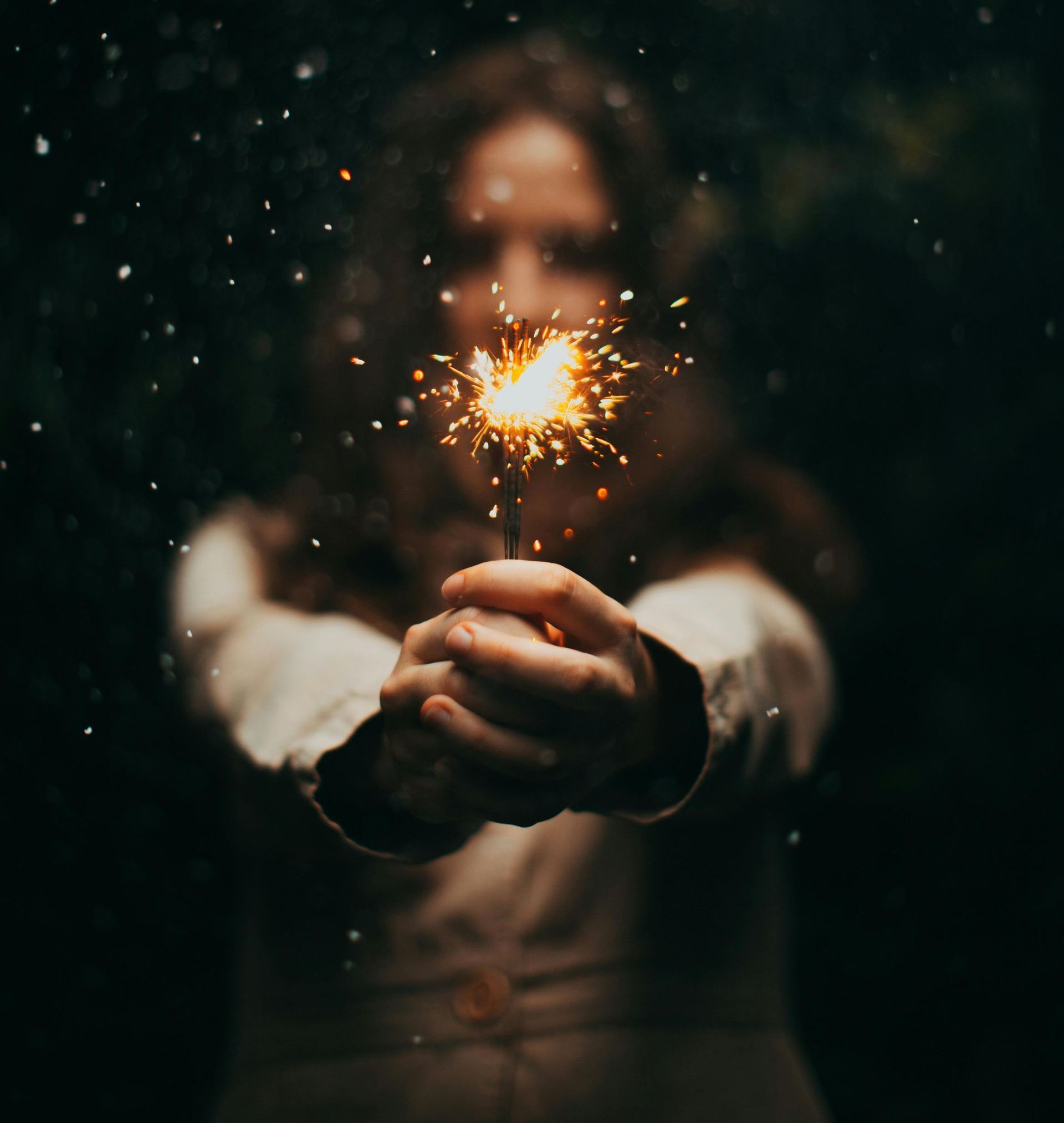 Una persona tiene in mano una stellina luminosa davanti a sé, contro uno sfondo scuro e sfocato con piccole particelle di luce.