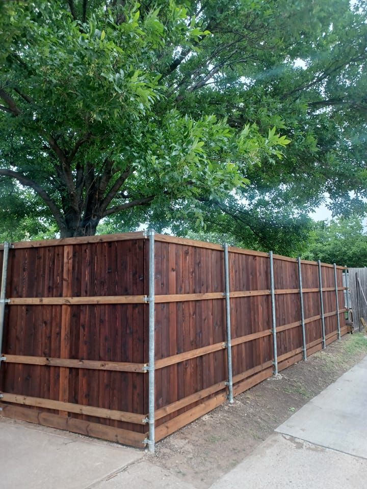 A wooden fence is sitting next to a tree on the side of a road.