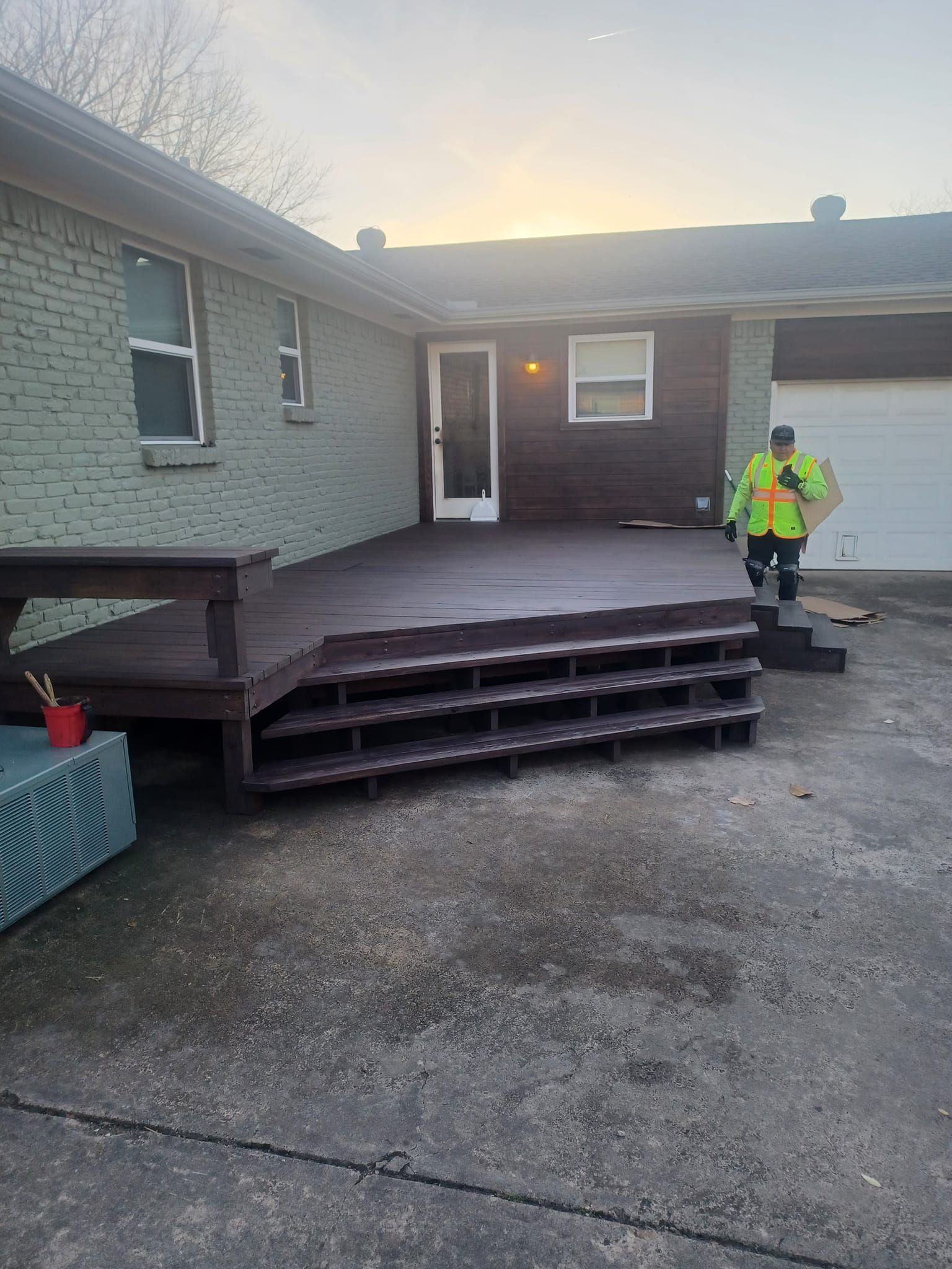 A man is standing in front of a house with a deck and stairs.