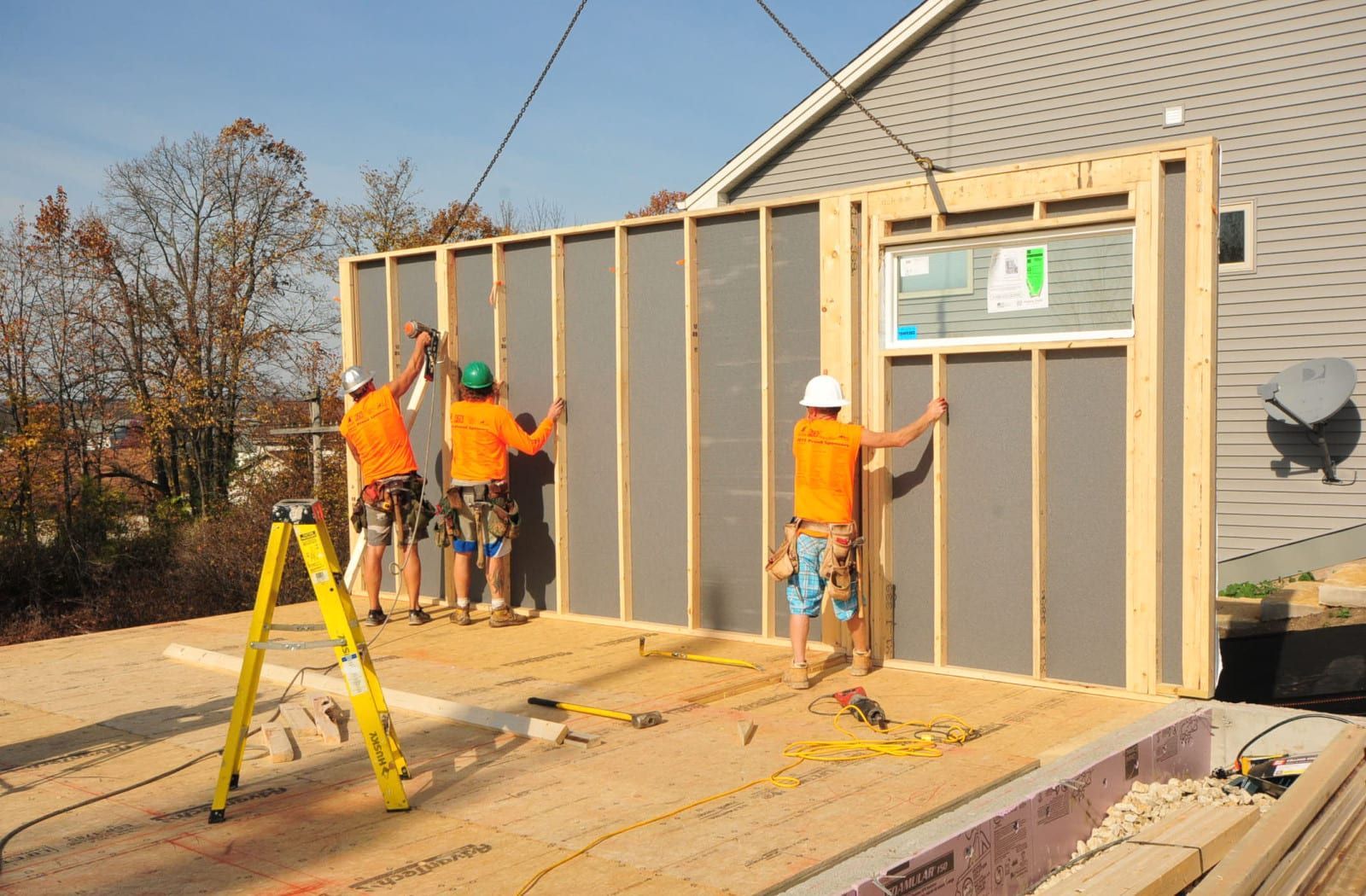 A group of construction workers are working on the side of a house.